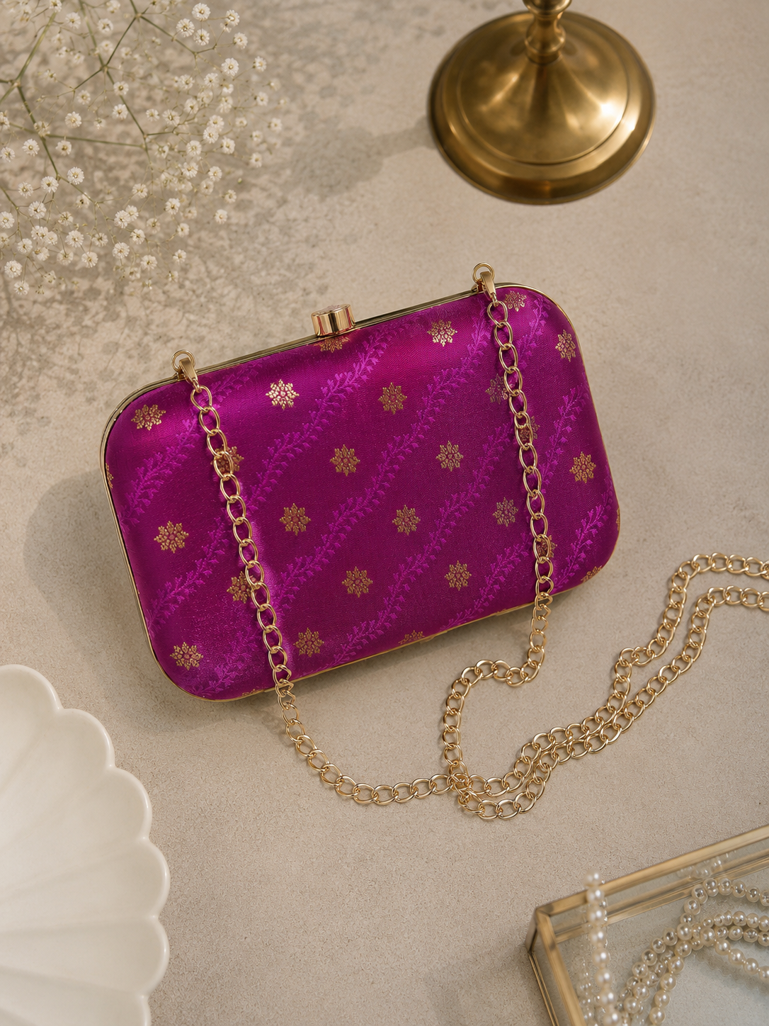 Magenta pink brocade clutch bag with floral butti patterns, detachable gold chain, and metallic frame for festive and wedding wear