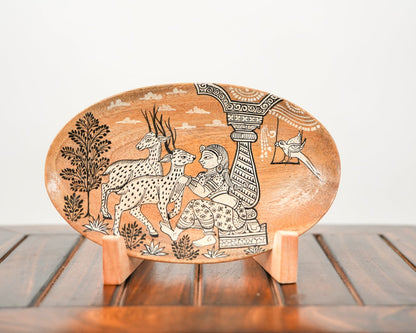 An oval hand-painted clay plate with traditional South Asian motifs, displayed on a small wooden stand on a wooden table against a white background.
